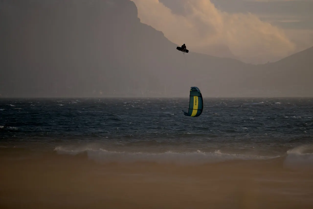 Kitesurfista em silhueta bem alto sobre o mar agitado ao entardecer, com montanhas ao fundo