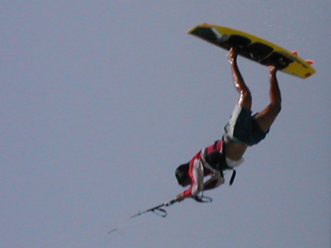 A kitesurfer in the air above choppy water, board still on the feet, lines running up to a kite out of frame.