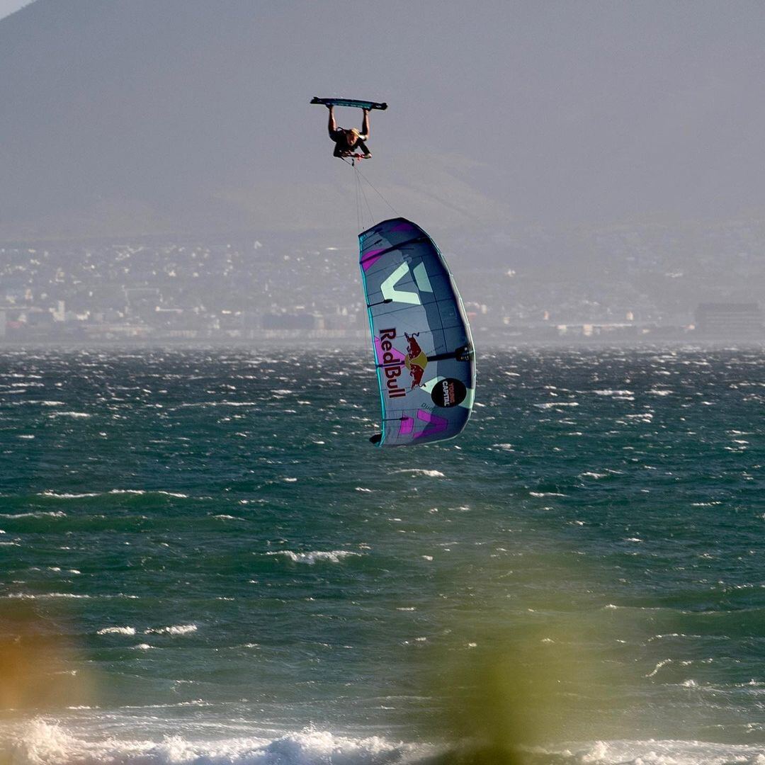 Kitesurfer performing a board-off megaloop trick high above Cape Town ocean with Red Bull branded kite