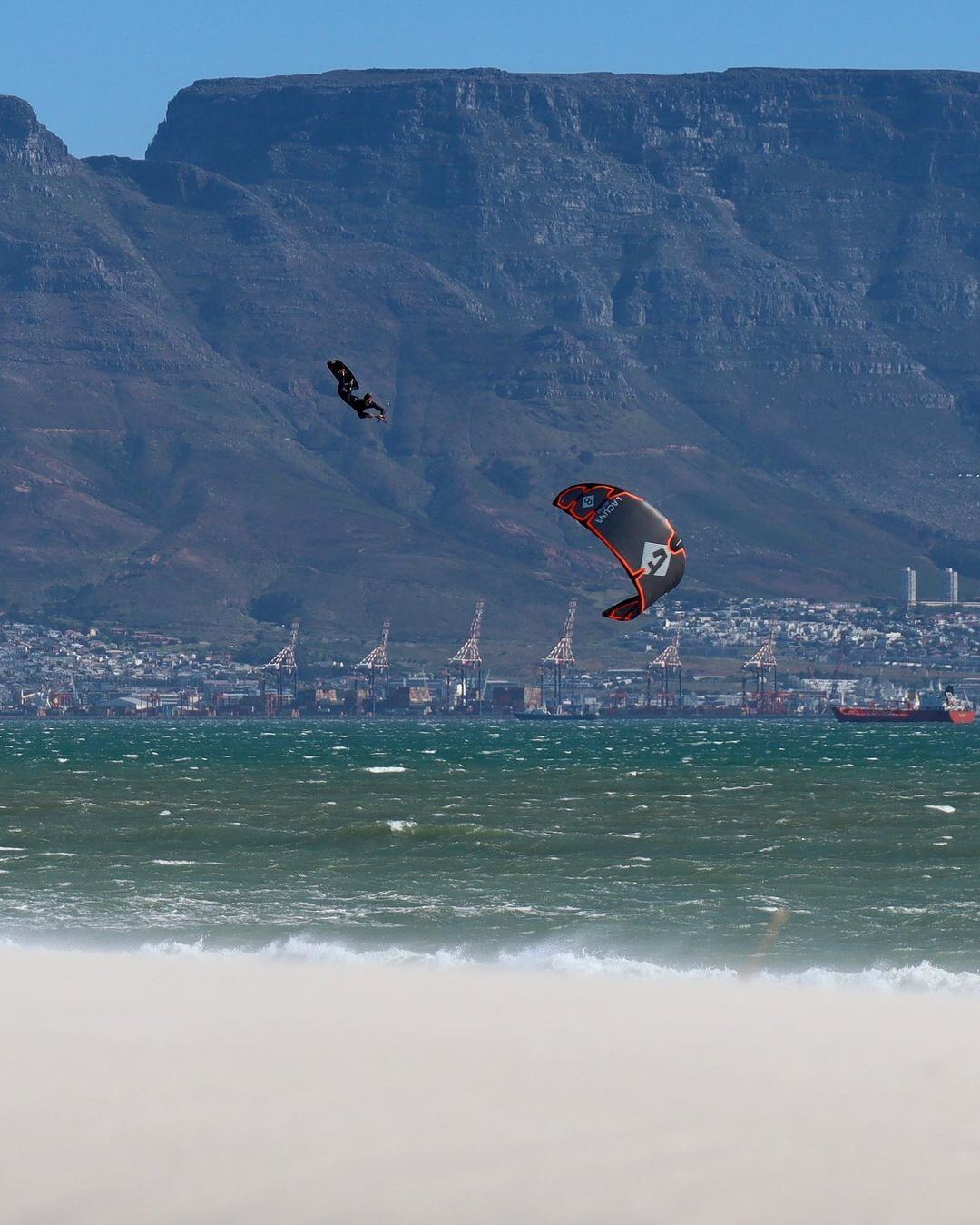 Two kitesurfers boosting big air in front of Table Mountain and Cape Town harbour