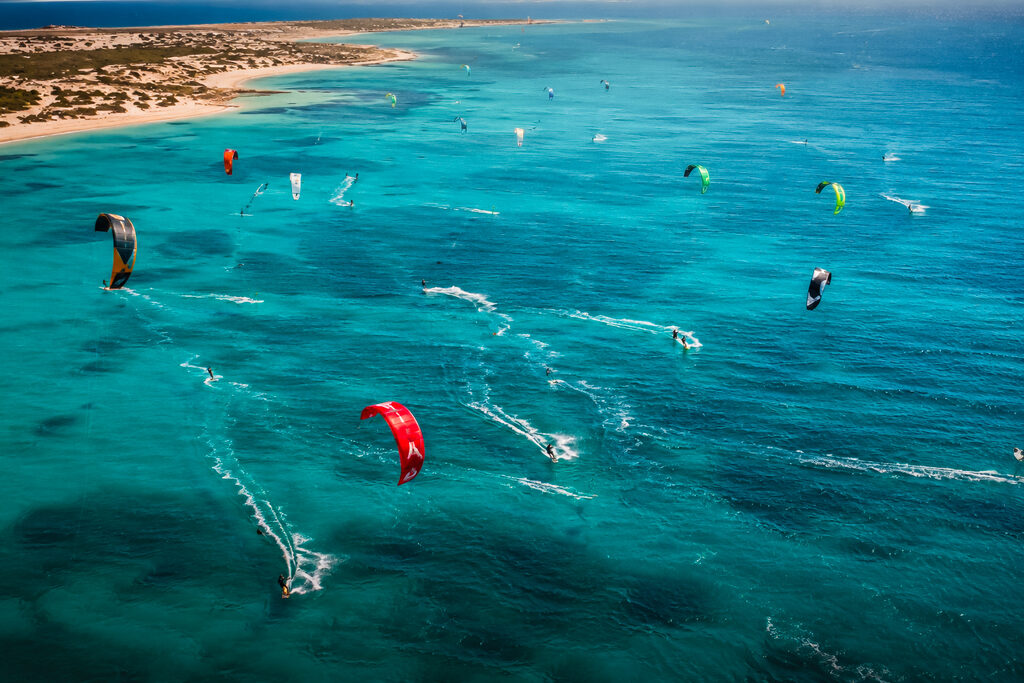 Aerial view of a turquoise lagoon with many kitesurfers and colourful kites